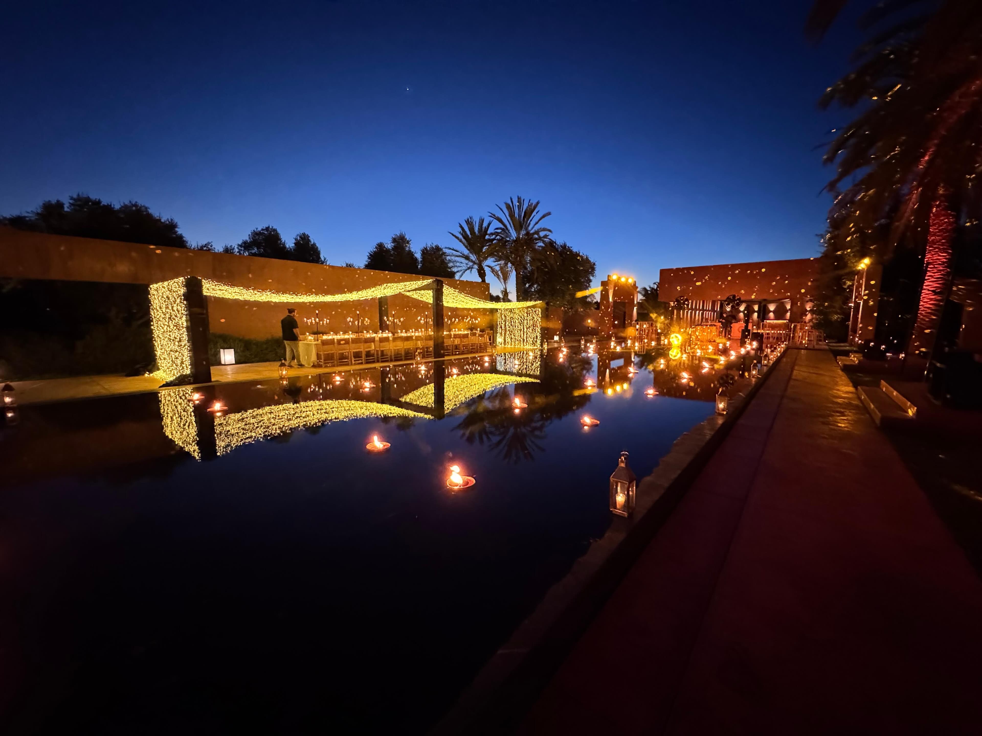 Dinner set beneath a pavilion of lights beside a candlelit pool at dusk