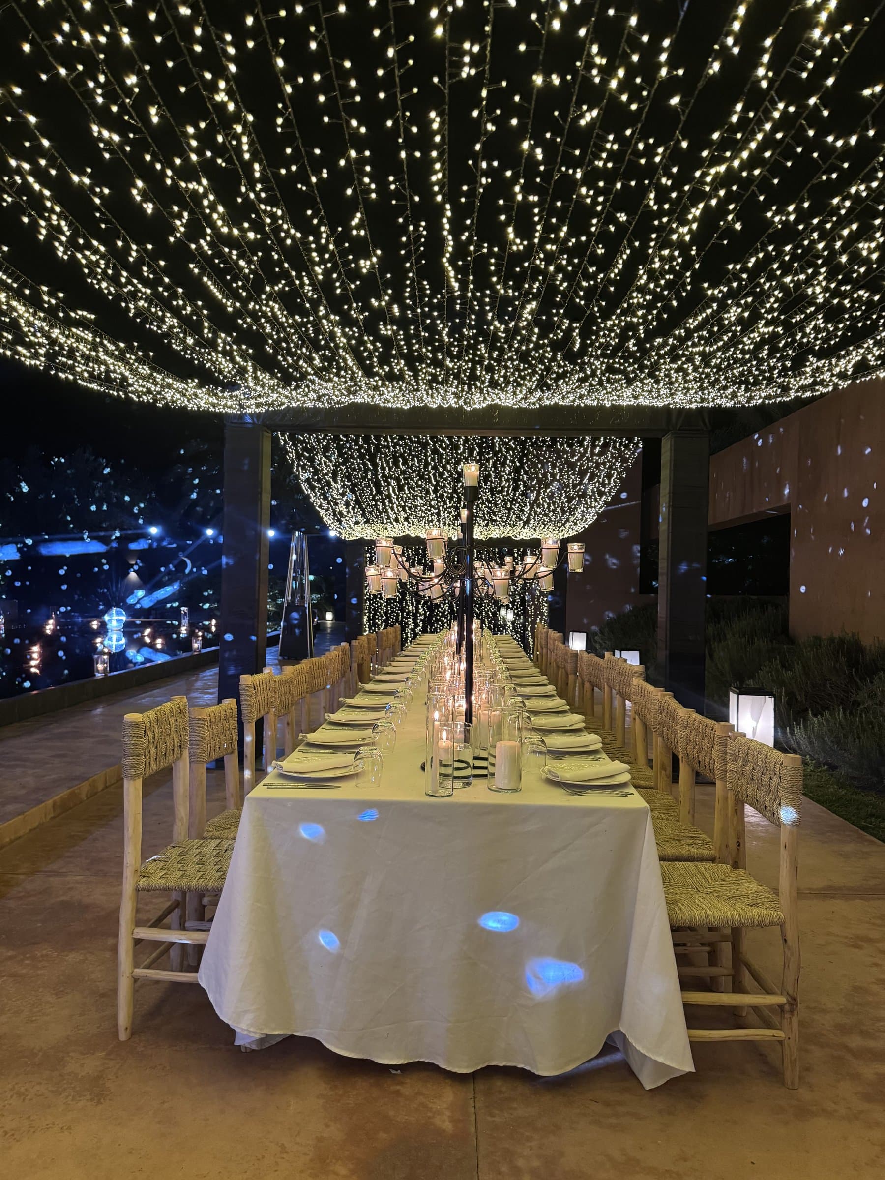 Long table set beneath a canopy of fairy lights, on a terrace overlooking the city at night