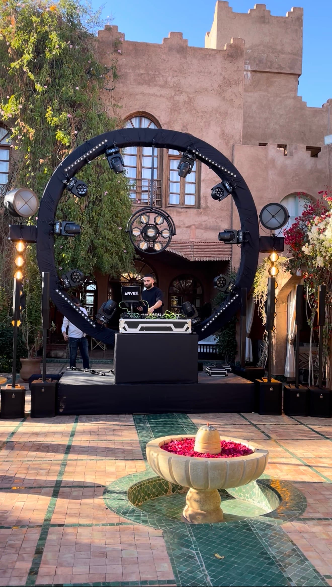 DJ at the decks, framed by a ring of spotlights in a kasbah courtyard