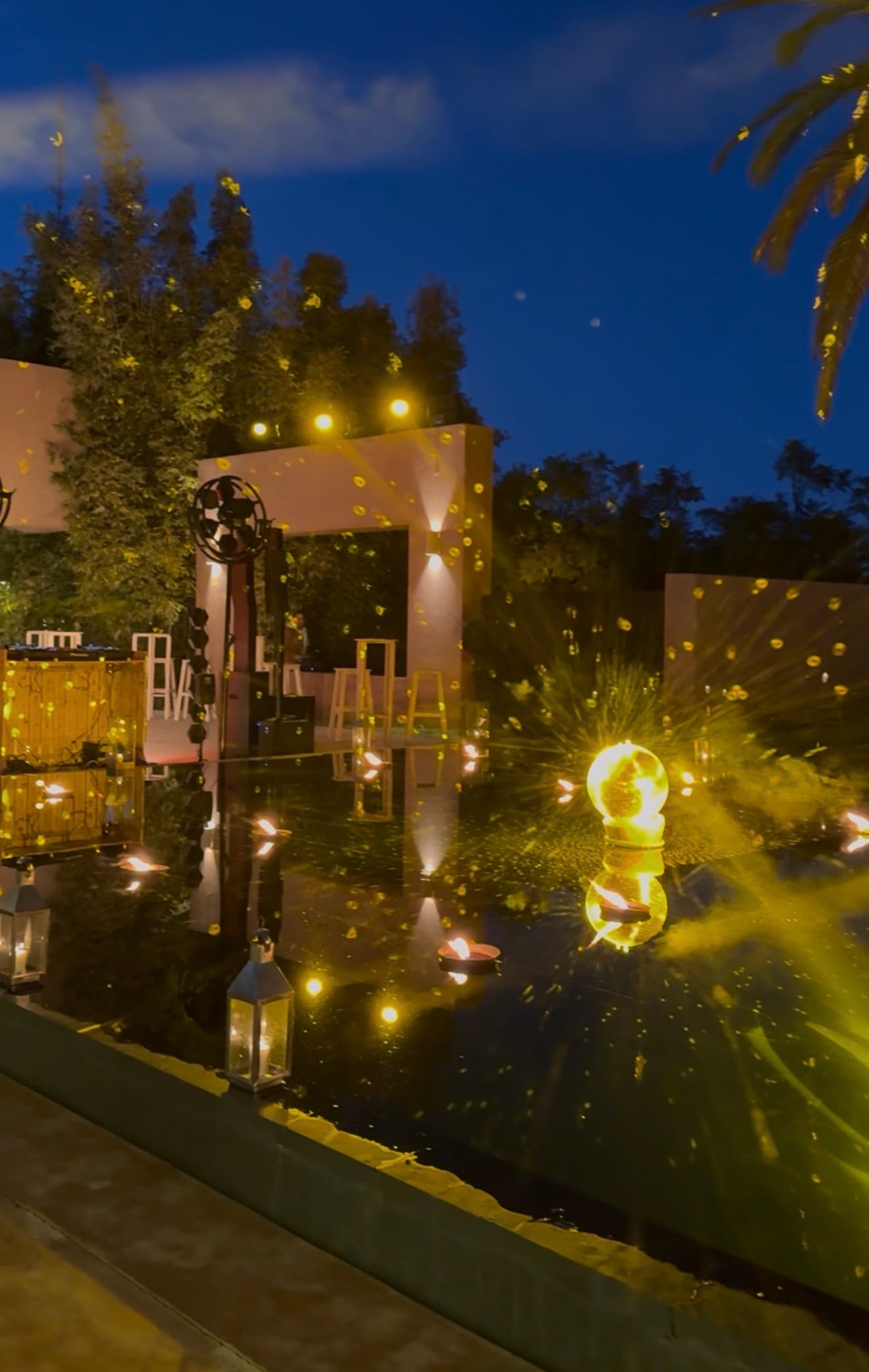 Pool lit by candles and lanterns beside a pavilion of lights at nightfall